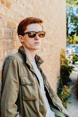 people man in green jacket leaning on brown brick wall person