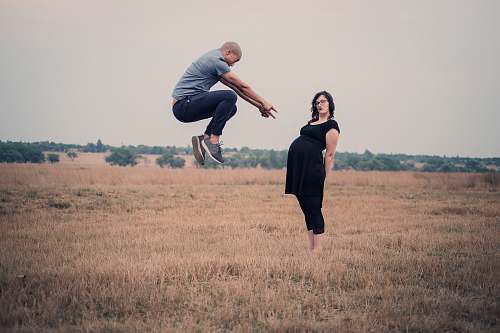 people man jumping in front of woman standing on field person