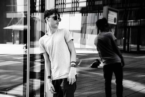 person man leaning on glass wall while looking on his right side black-and-white