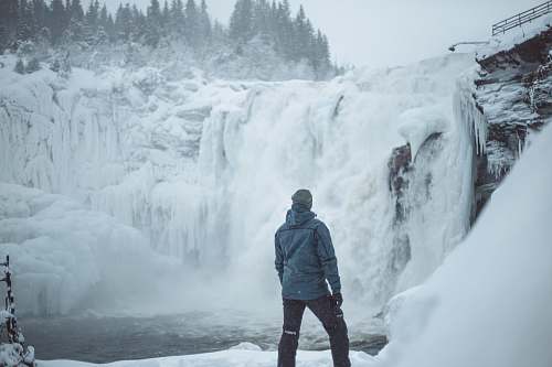 people man standing near snow covered falls during daytime person