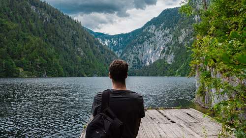 people man standing on brown wooden board near body of water surrounded by mountains back