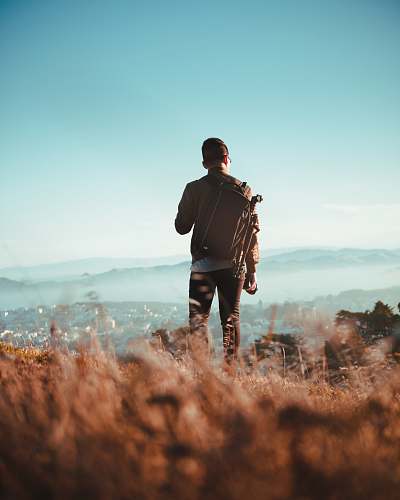 person man standing on dried grass field while watching aerial view of village at daytime people