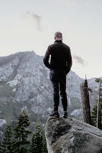 people man standing on gray rock looking at mountain peak person