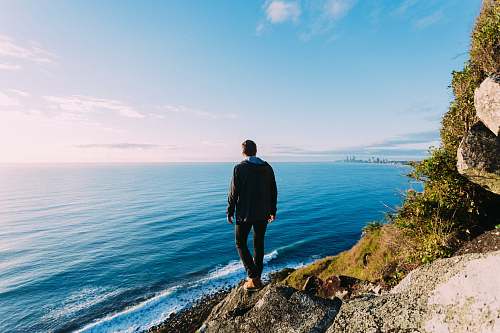 people man standing on rock cliff near sea person