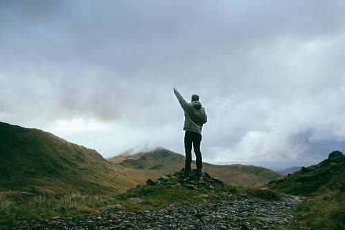 people man standing on rocks near mountains pointing sky during daytime person