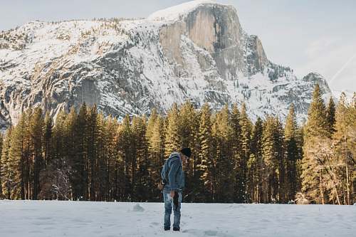 people man standing on snow field near trees and mountain during day person