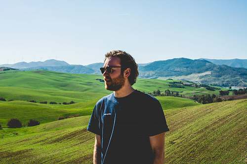 people man wearing black crew-neck t-shirt standing near hill at daytime person