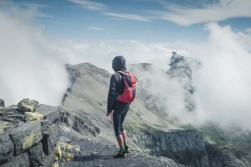 people man wearing black hooded jacket and backpack standing on rocks facing clouds person
