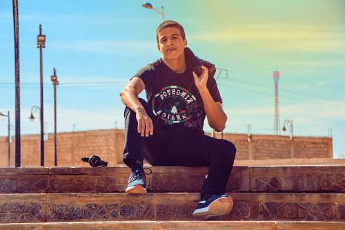 people man wearing black Kingston t-shirt sitting on stair while holding hoodie person