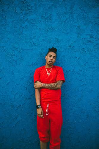 people man wearing red crew-neck t-shirt and drawstring pants leaning on blue wall person