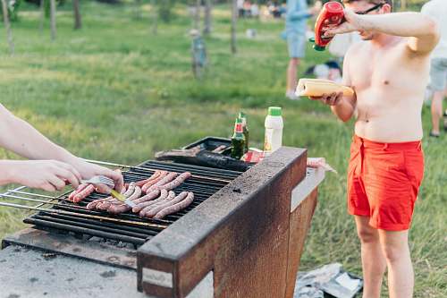 people man wearing red shorts standing at grill putting ketchup on hotdog bbq