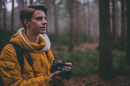 person man wearing yellow parka jacket holding DSLR camera photographer