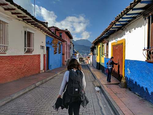 person person in gray shirt with backpack walking on street between houses people