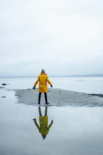 people person in yellow coat on gray sand surrounded by water person