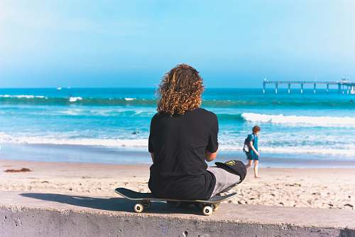 people person sitting on skateboard with sea shore background person