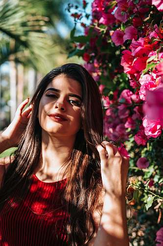 people selective focus photography of woman wearing red crew-neck sleeveless top beside pink flowers person