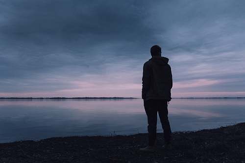 people silhouette of man standing near body of water person
