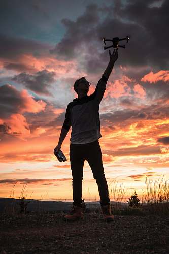 people silhouette photo of man holding up drone person