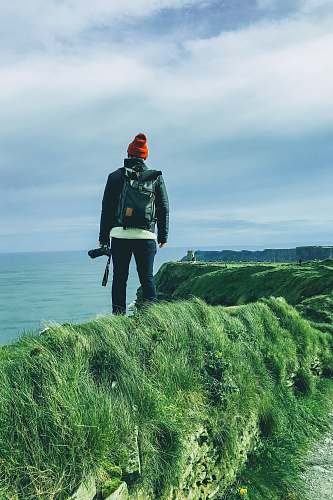 people standing man holding DSLR camera on cliff looking to ocean under white sky person
