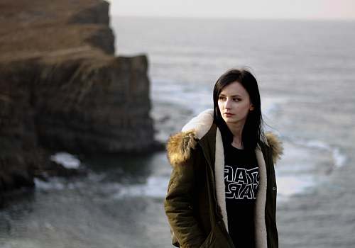people woman in brown parka jacket standing on rock formation person
