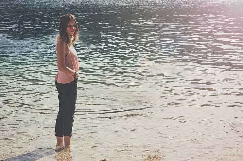people woman in pink sleeveless top and black cargo pants standing on body of water person