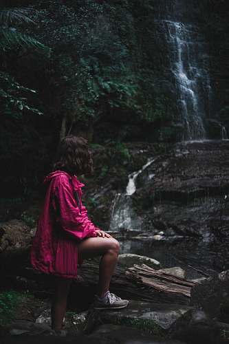 people woman in purple jacket standing near waterfalls person