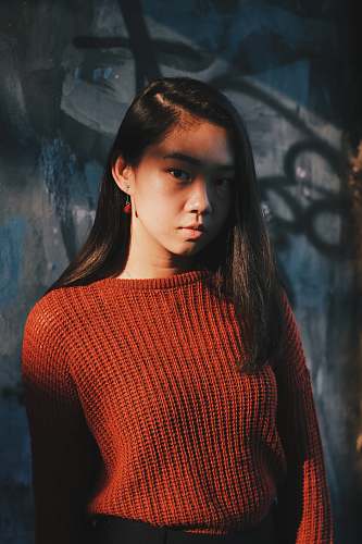 person woman in red sweater posing near gray wall people