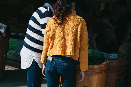 people woman in yellow knit sweater and blue denim jeans stands beside man person