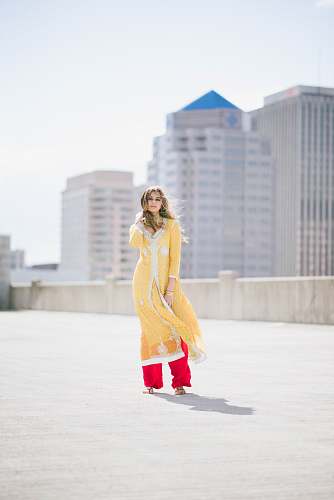 people woman in yellow shalwar kameez standing on concrete floor holding her hair during daytime person