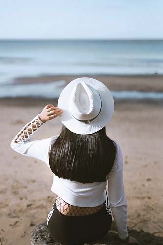 person woman sits on rock watching ocean hat