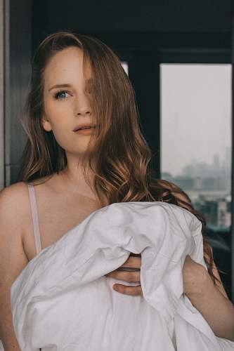person woman standing against the wall holding white blanket inside room people