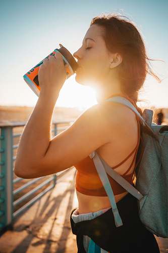 people woman standing and drinking near gray metal rail during daytime person
