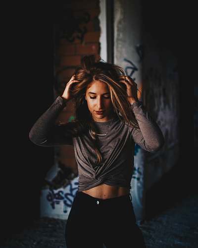 person woman standing near gray concrete wall while holding her hair people
