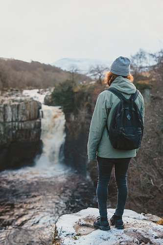 people woman standing on cliff facing waterfall person