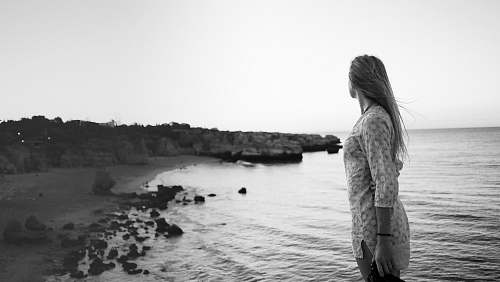 people woman standing on seashore grayscale photography black-and-white