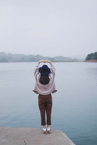 person woman taking a heart pose beside body of water people
