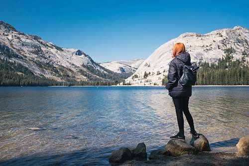people woman wearing black bubble jacket beside lake near hills covered with snow during daytime person