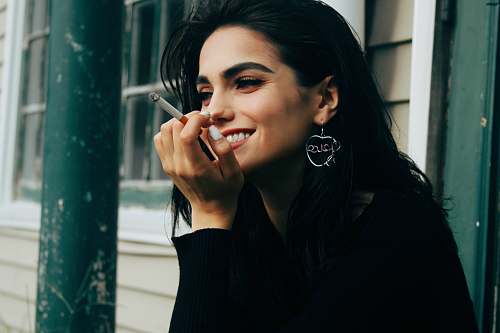 people woman wearing black long-sleeved shirt holding lighted cigarette while smiling person
