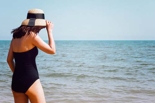 people woman wearing black onepiece swimsuit standing beside seashore at daytime person