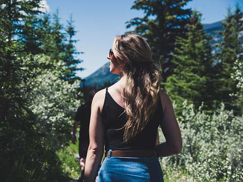people woman wearing black spaghetti strap crop top standing in front of trees while looking left side during daytime person