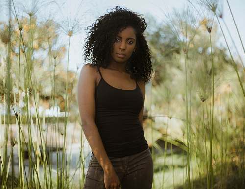 people woman wearing black spaghetti strap top standing near plants person