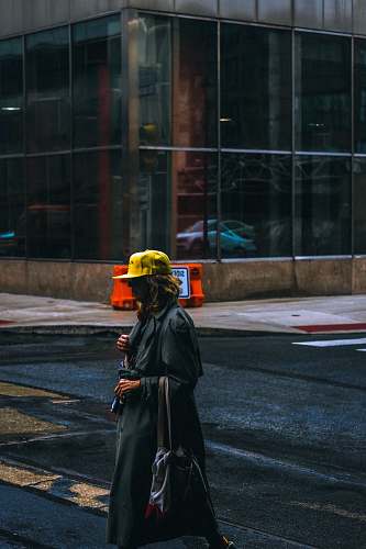 people woman wearing black trench coat and yellow cap walking on street person
