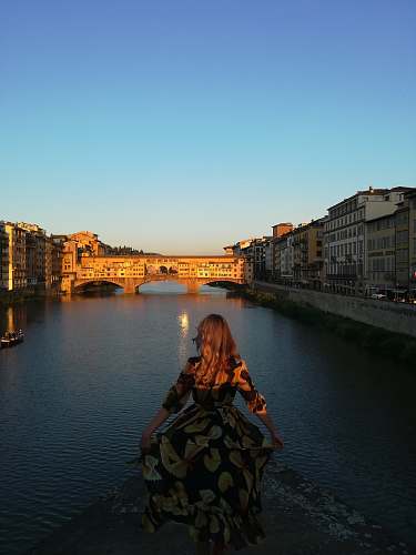 people woman wearing brown and black floral 3/4-sleeved dress standing beside river person