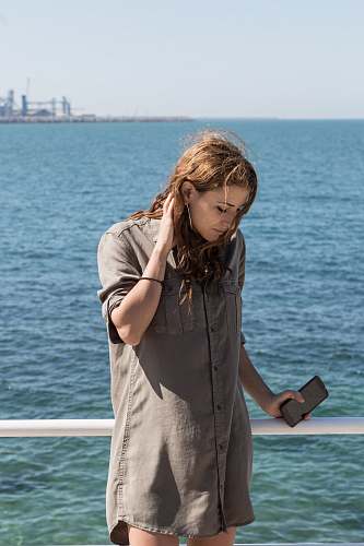 people woman wearing brown button-up long-sleeved dress beside large body of water during daytime person