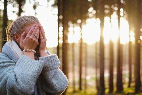 people woman wearing gray coat with hands on her face during daytime person