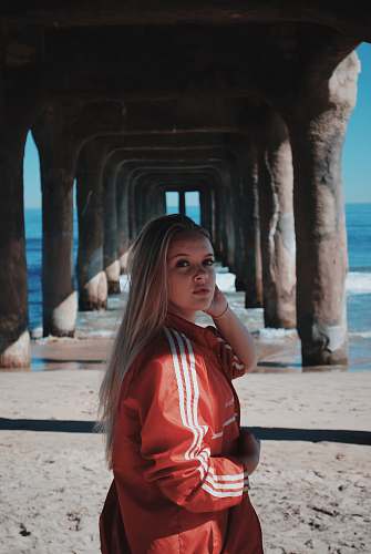 people woman wearing red adidas zip jacket underneath pier during daytime person