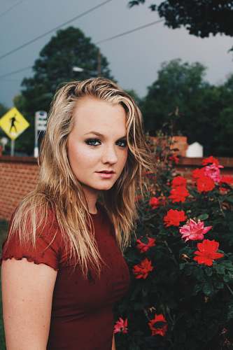 person woman wearing red shirt standing near red petaled flower people
