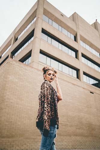 people woman with hand on hair standing in front of brown wall person