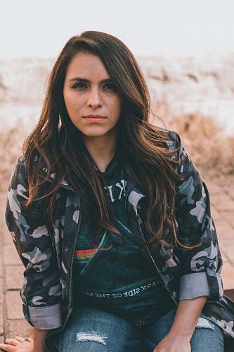 people women's black, white, and green camouflage zip-up jacket sitting on concrete floor person