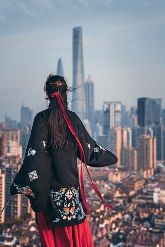 human black haired woman in black coat staring at building during daytime person